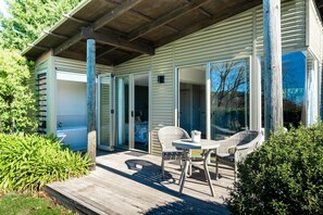 A wooden deck with wicker furniture, a bathtub, and sliding glass doors leading to a room.