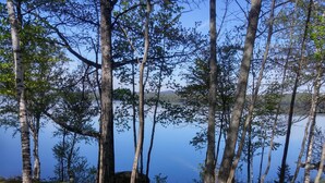 A wooden picnic table with two red Adirondack chairs, set on grass with trees and a lake in the background.