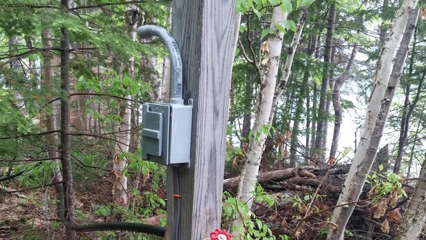 A wooden utility pole with a metal box and a red valve in a forested area.