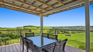 A covered outdoor area with a table and chairs, overlooking a green landscape. - Bunya@Maleny Farm House (Witta)