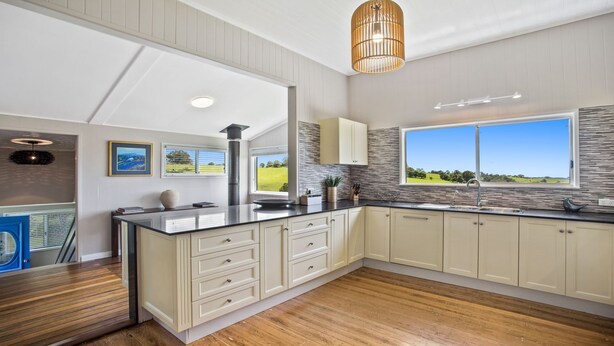 A modern kitchen with a large island, wooden flooring, and a view of the outdoors. - Bunya@Maleny Farm House (Witta)