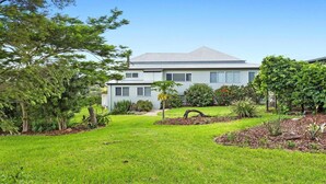 A two-story house with a sloped roof, surrounded by a well-maintained lawn and various shrubs. - Bunya@Maleny Farm House (Witta)