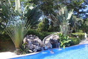 A swimming pool with a waterfall feature, surrounded by tropical plants and rocks. - Luxury condo, Club del Cielo, Jaco, Costa Rica (Jacó)