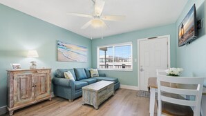 A room with a blue couch, a wooden cabinet, a white chair, a small table, and a ceiling fan.