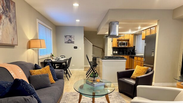 A modern living room with a grey sofa, a glass coffee table, and a dining area with a black table and chairs. - Heart of the City Group Hub • Patio • Fireplace • Parking (Chicago)