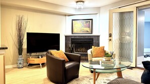 A modern living room with a fireplace, leather sofa, glass coffee table, and a flat-screen TV. - Heart of the City Group Hub • Patio • Fireplace • Parking (Chicago)