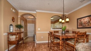Zona de menjador amb taula i cadires de fusta, llum penjant i un quadre al mur.