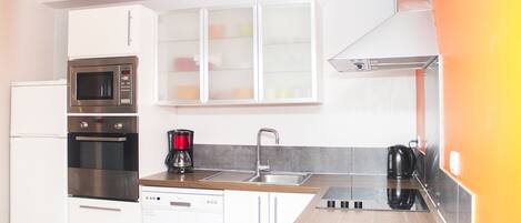 A modern kitchen with white cabinets, stainless steel appliances, a wooden countertop, and a built-in oven.