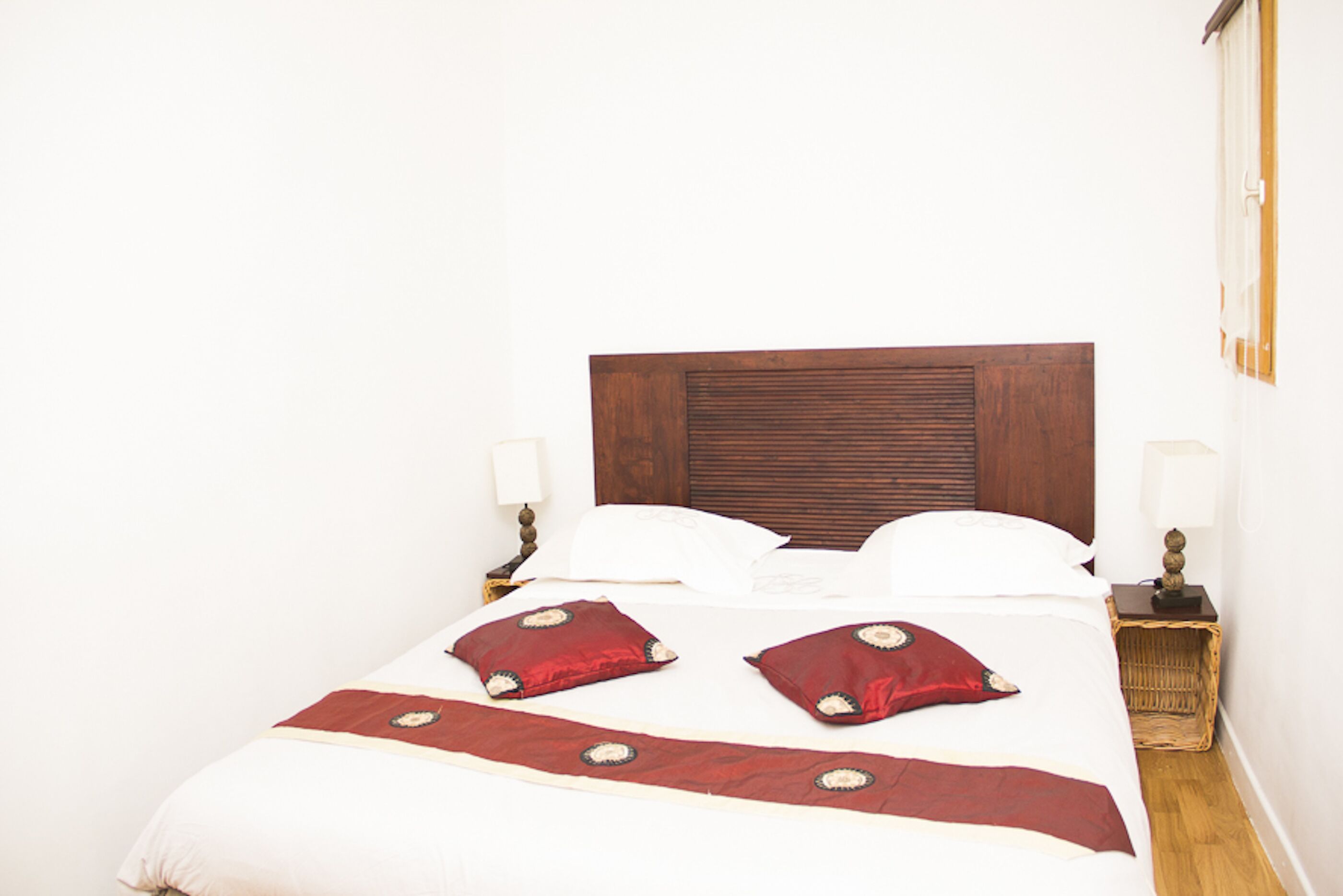 A neatly made bed with a wooden headboard, two bedside lamps, and a red throw blanket.