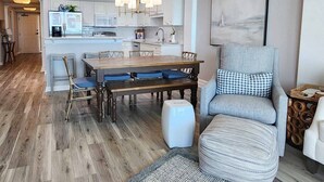 A modern kitchen with white cabinets, a dining table with blue cushions, and a grey armchair. - Crescent C4B - Nicely Furnished - Oceanfront - Private Balcony (Pawleys Island)