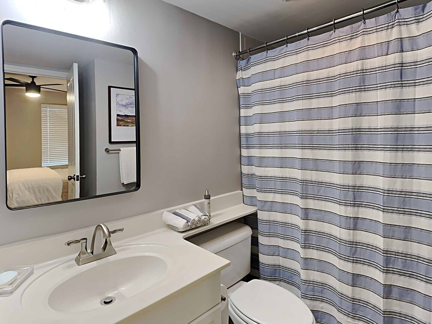 A bathroom with a white sink, a mirror, a toilet, and a striped shower curtain.