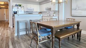 A modern kitchen with white cabinets, a wooden dining table with blue cushions, and a chandelier. - Crescent C4B - Nicely Furnished - Oceanfront - Private Balcony (Pawleys Island)