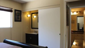 Un dormitorio con cama, un baño con lavabo y espejo, y un pasillo que lleva a otra habitación.