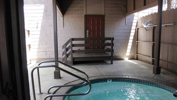 Una piscina interior con cubierta de madera, una escalera metálica y una puerta roja al fondo.