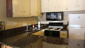 Una cocina con armarios blancos, estufa, microondas y refrigerador.