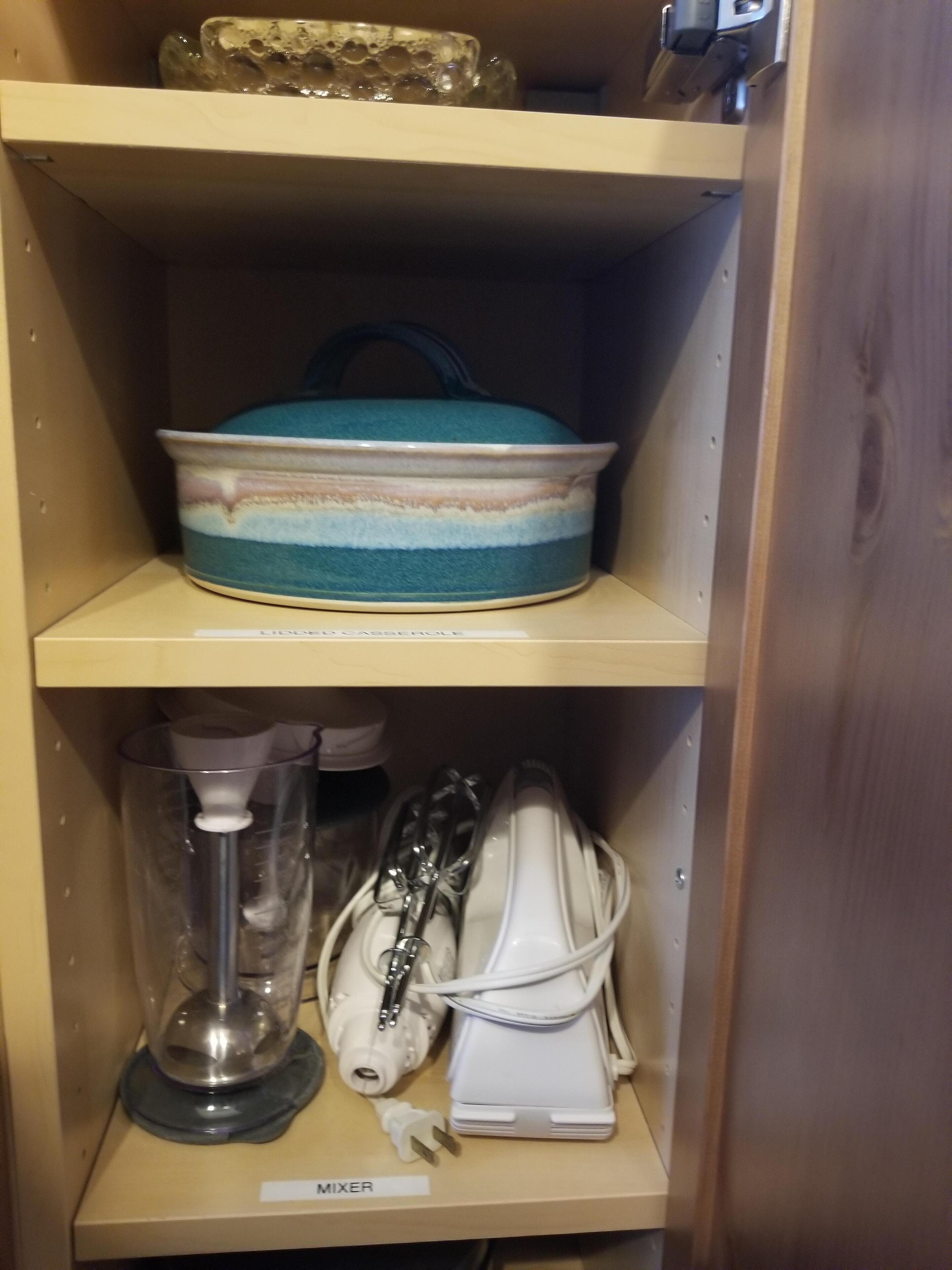 A shelf with a ceramic pot, a blender, and a mixer on a wooden cabinet.