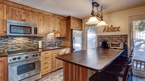 A kitchen with wooden cabinets, stainless steel appliances, a large island, and a 'Relax' sign.
