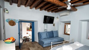 Un dormitorio con cama, sofá azul, comedor con mesa y sillas, y cocina con frutero.