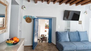 Una sala de estar con un sofá azul, un televisor montado en la pared, una zona de comedor con mesa y sillas, y un sombrero decorativo en la pared.
