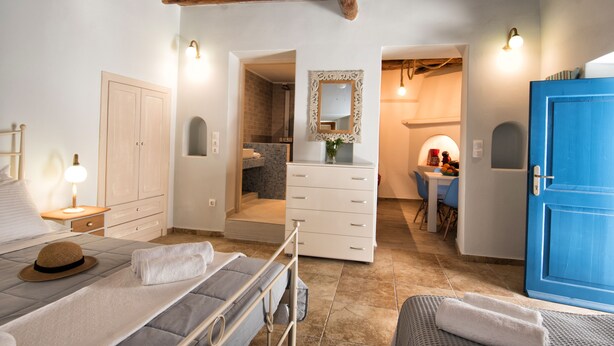 Un dormitorio con cama, mesita de noche y armario. Se ve un baño a través de una puerta abierta.