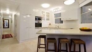 A modern kitchen with white cabinetry, a large island with stools, and a fruit bowl on the counter.