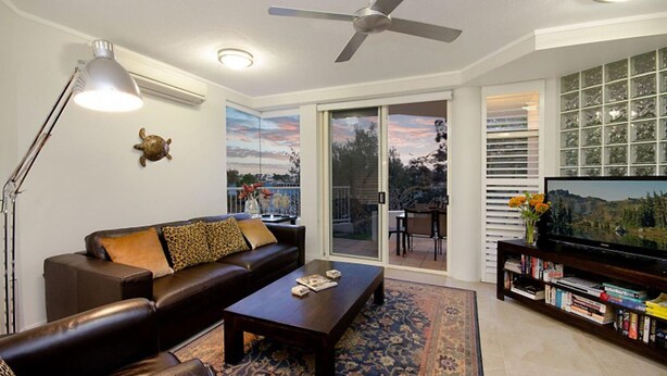 A living room with a sofa, coffee table, TV, bookshelf, and a view through the glass door.