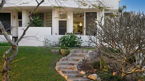 A modern house with a stone staircase leading to the front door, surrounded by a well-maintained lawn and a variety of plants.