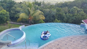 A swimming pool with a hot tub, surrounded by lush greenery and a view of the countryside.