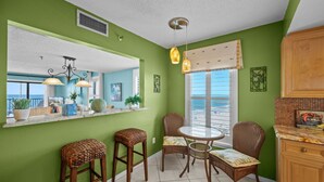 Une cuisine avec un mur vert, une grande fenêtre donnant sur un beau paysage, des chaises en osier et une table à manger.
