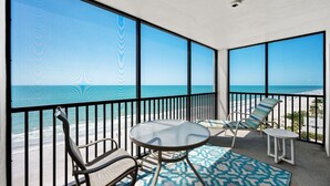 Un balcon avec vue sur la plage, une table, deux chaises et un petit tapis.