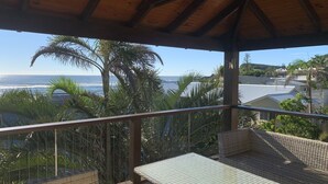 Uma área externa coberta com vista para o oceano, palmeiras e um edifício ao fundo.