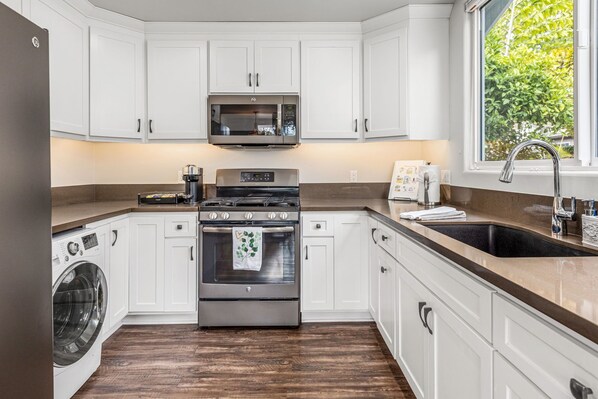 A modern kitchen with white cabinets, a stainless steel oven, a microwave, and a large window.