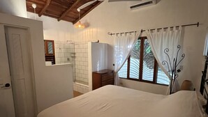 Een slaapkamer met een bed, een plafondventilator, een raam met gordijnen, een houten plafond en een betegelde vloer.