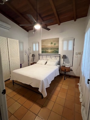 Un dormitorio con cama, ventilador de techo, un cuadro y una mesita de noche.