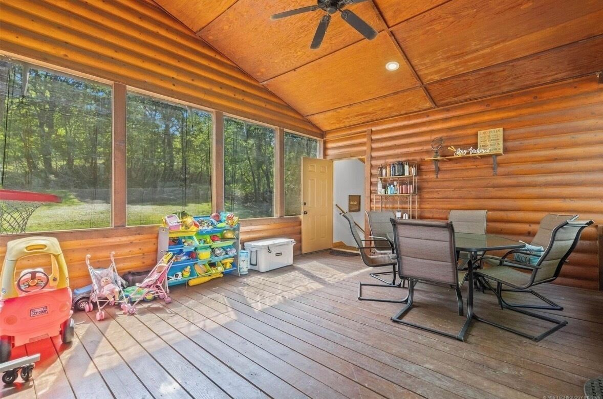 A wooden cabin interior with a dining area, bookshelves, and a view of the forest.