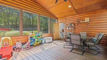 A wooden cabin interior with a dining area, bookshelves, and a view of the forest.