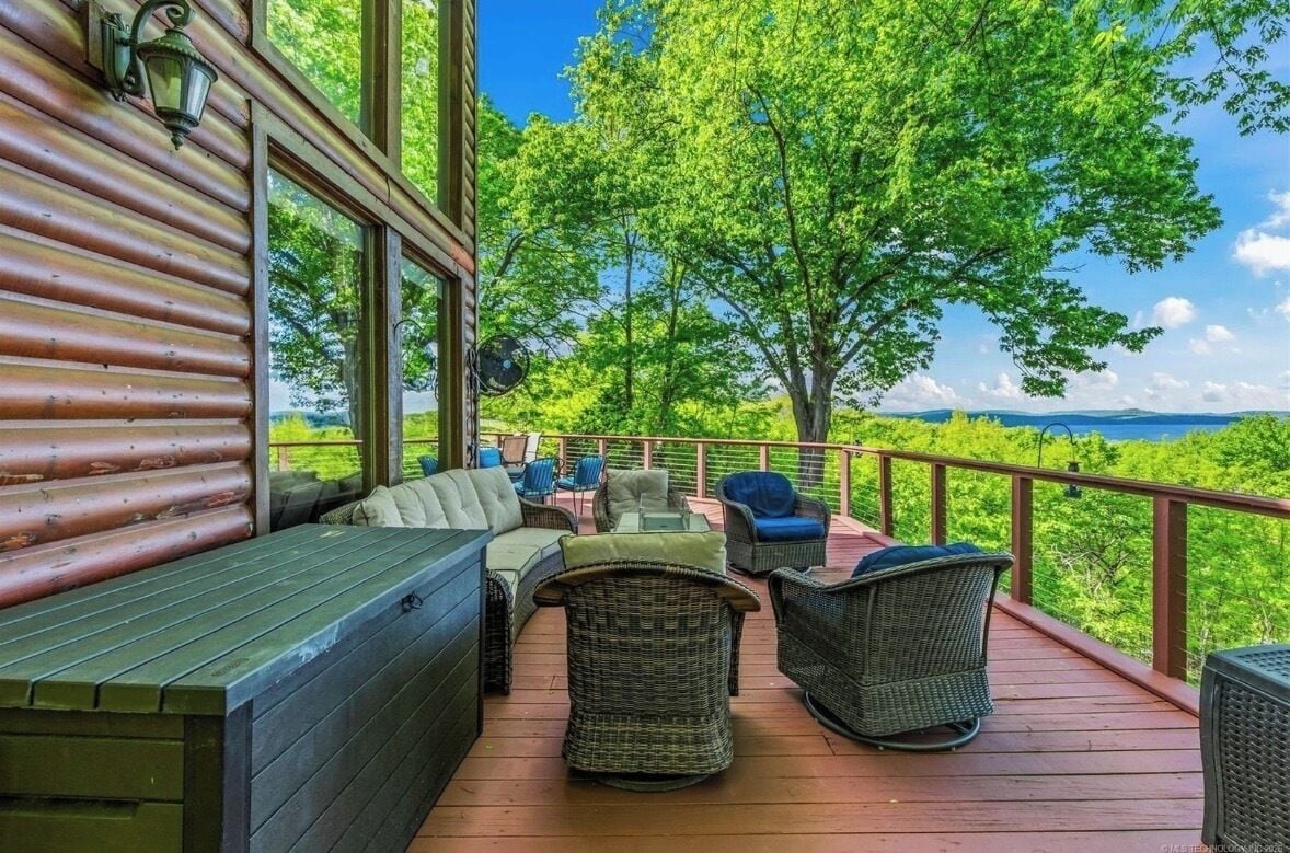 A wooden deck with outdoor seating, a view of a forest, and a clear sky.