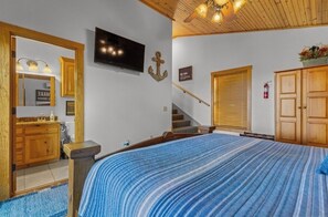 Un dormitorio con una cama, un televisor montado en la pared, una escalera de madera y una puerta de madera.