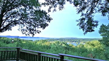A wooden deck with a railing overlooking a lake surrounded by dense forest and hills.