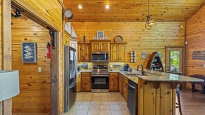 A wooden cabin interior with a kitchen featuring a central island, built-in appliances, and a clock on the wall.