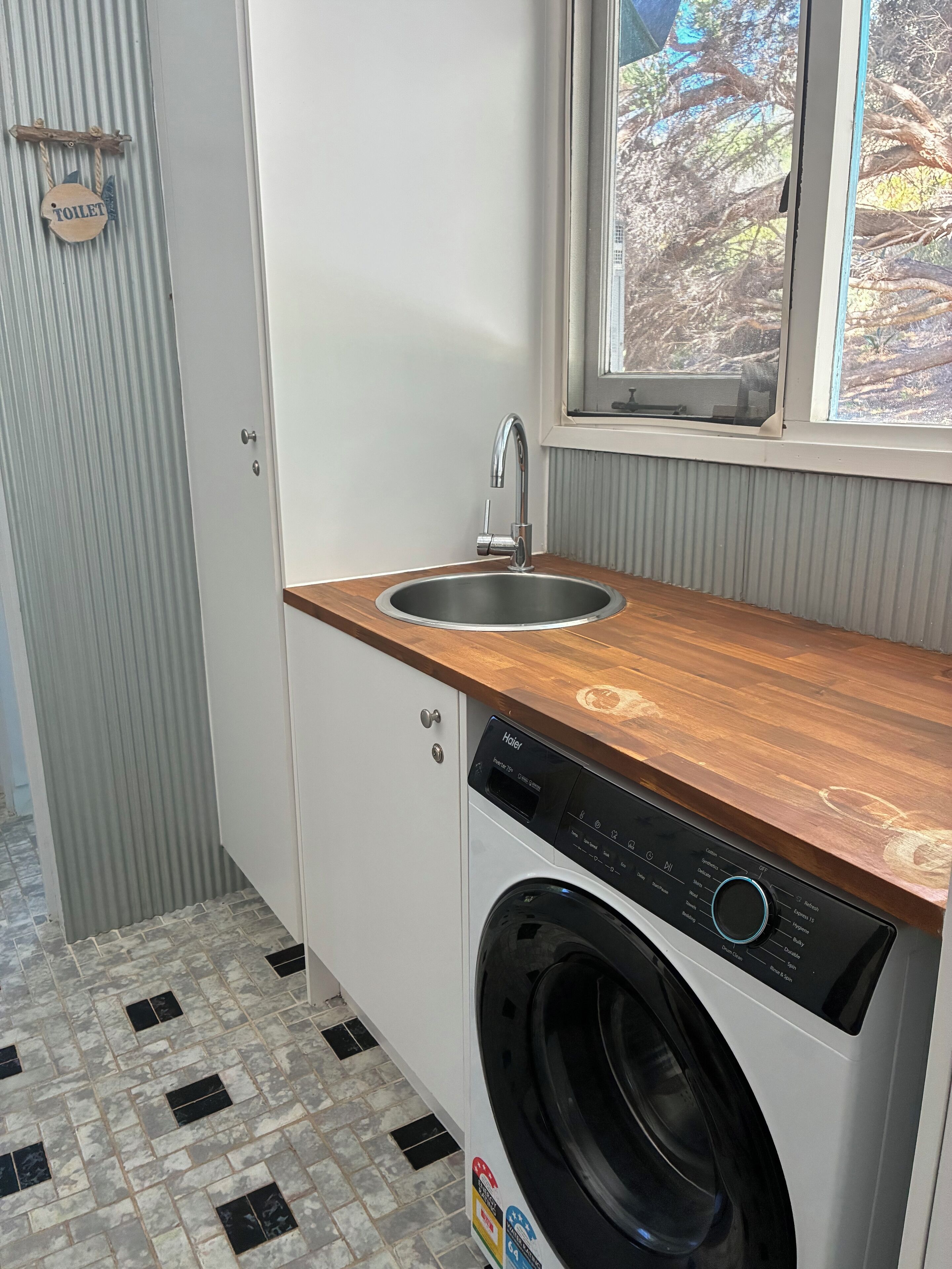 A compact laundry room with a washing machine, a sink, and a window.