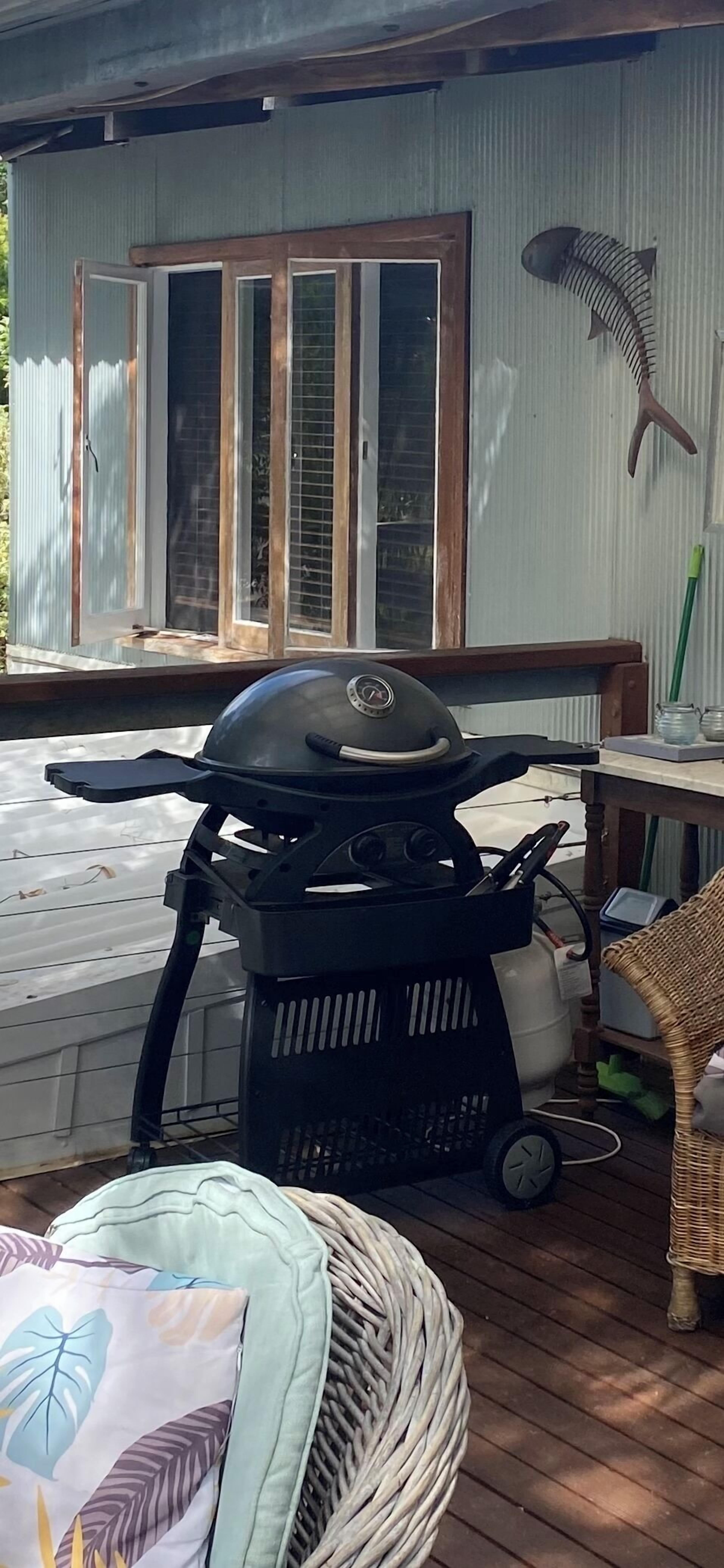 Una parrilla para barbacoa en una terraza de madera, con una silla de mimbre y un asiento acolchado cerca.