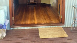 Ein Zimmer mit Holzboden, einem kleinen Holztisch mit einem Radio, einem grünen Sofa und einer Holztür mit dem Schild "THE TR".