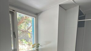 Ein kompakter Waschraum mit integrierter Waschmaschine und Trockner, einer Holz Arbeitsplatte, einem Waschbecken und einem Fenster mit Blick auf Grünfläche.