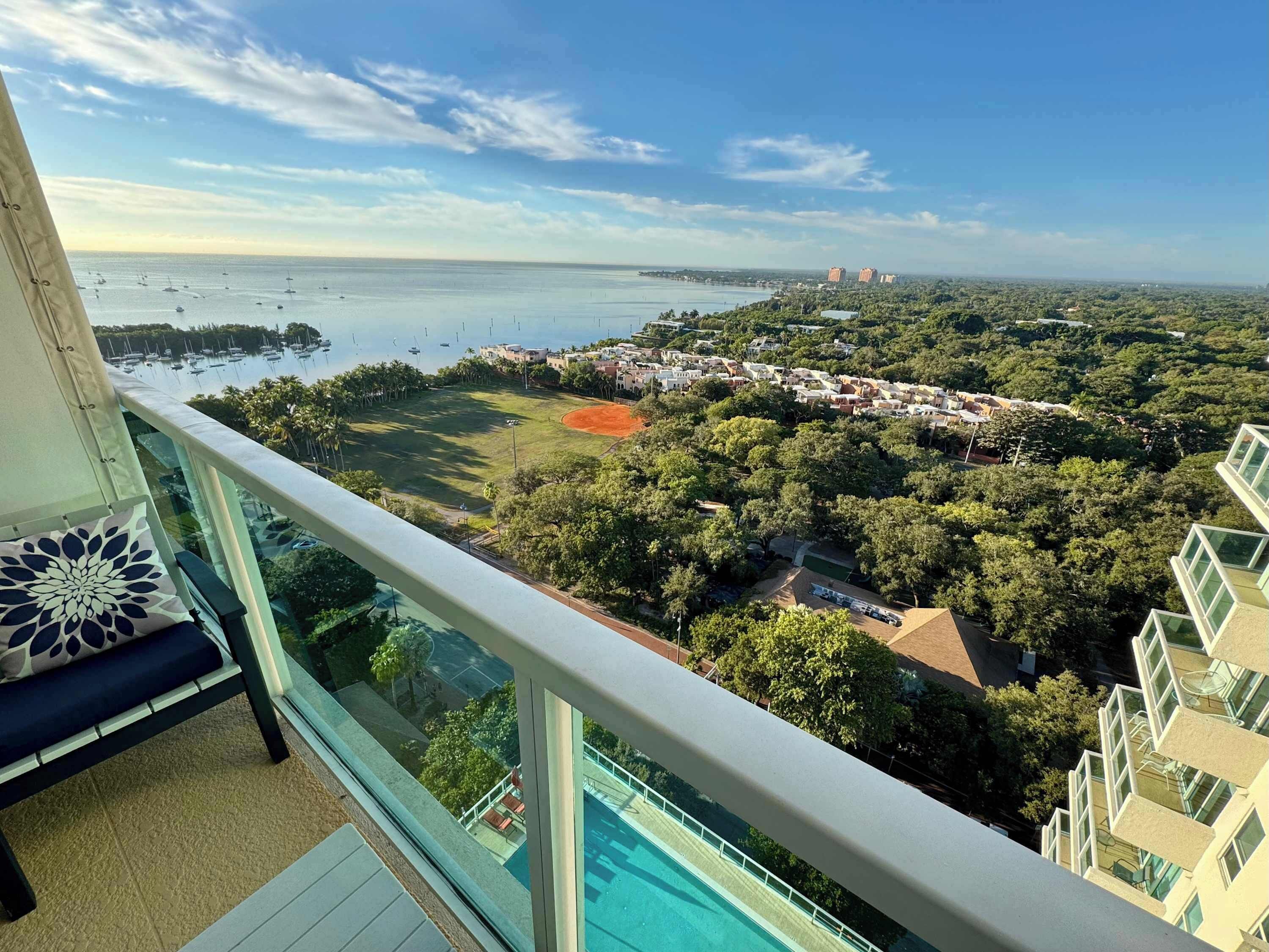 Un balcón con vista a un puerto deportivo, un campo verde y edificios residenciales.