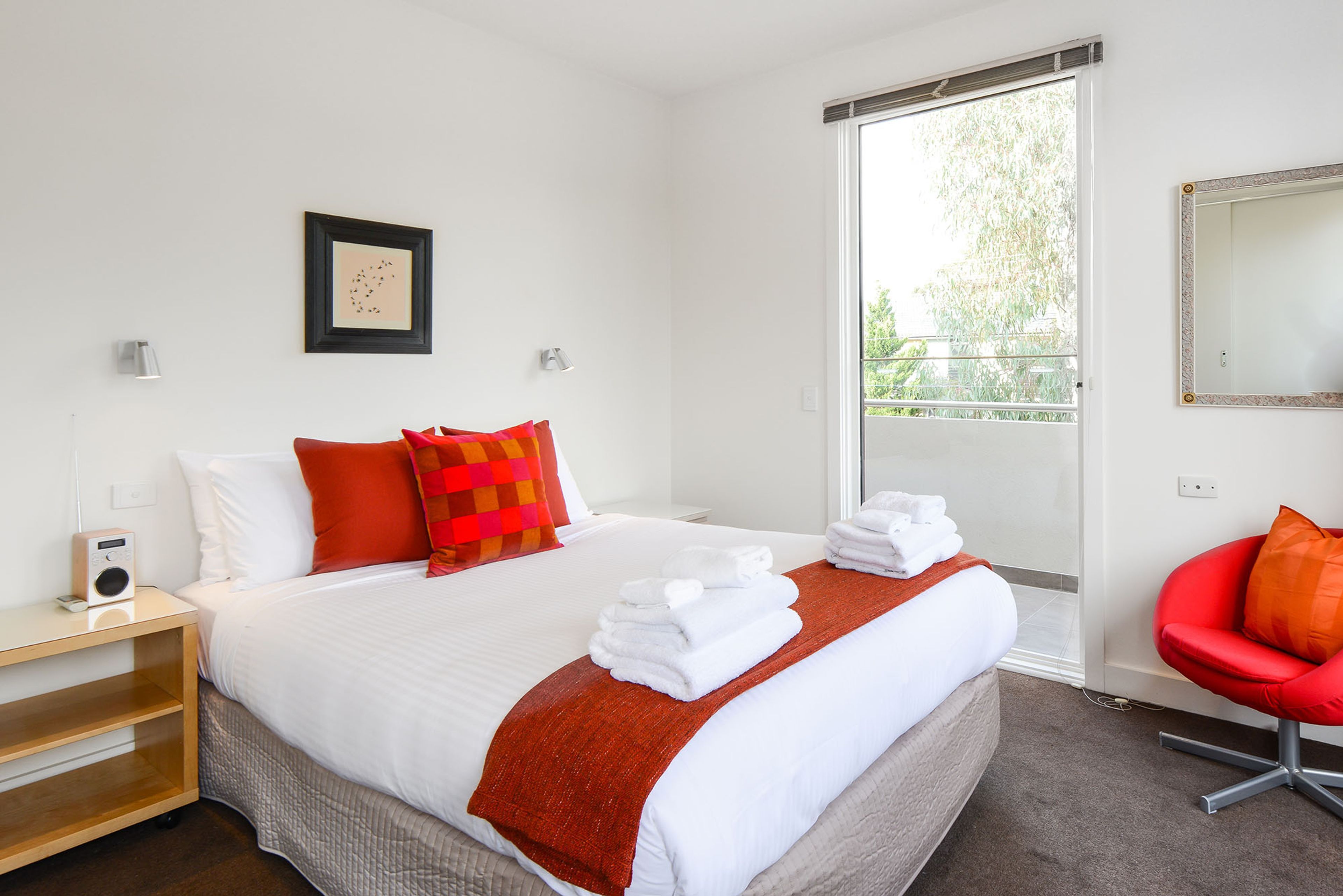 A hotel room with a bed, a chair, a bedside table, a mirror, and a window.
