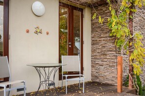 A patio with a glass table and a chair, a stone wall, and a door with glass panels.