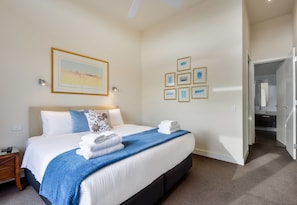 A hotel room with a large bed, a bedside table, a nightstand, a wall with framed pictures, and a door leading to another room. - Maple on Kent Pet Friendly Glen Iris Retreat (Glen Iris)