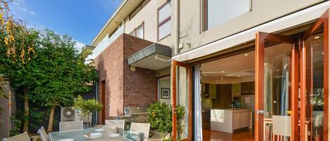 A modern house with a patio, a barbecue grill, and a glass door leading to a kitchen.