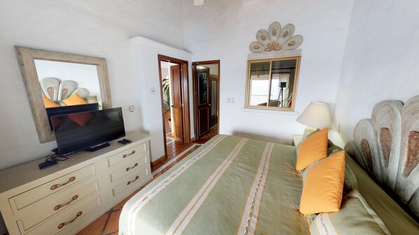Un dormitori amb un llit, una televisió sobre una petita taula, un mirall i una finestra.